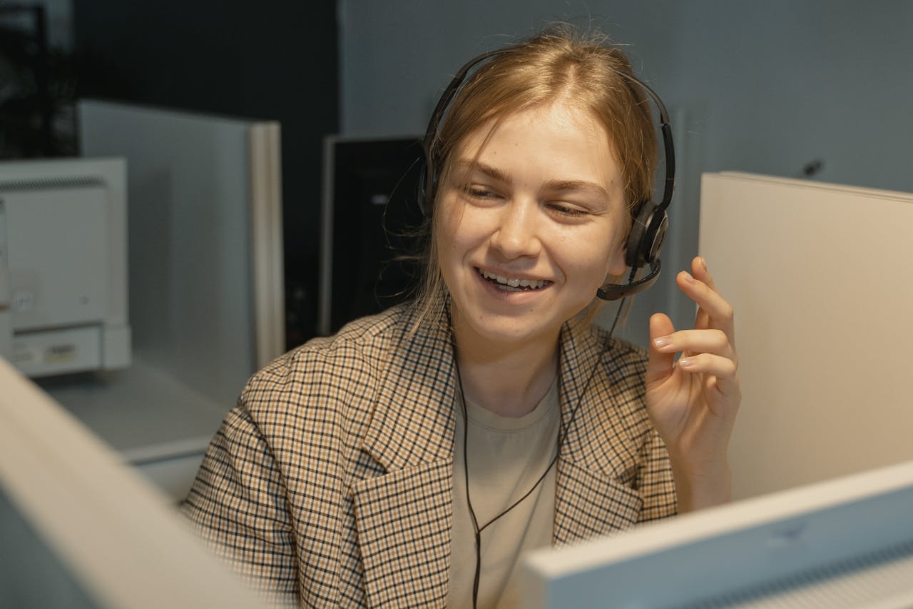 Smiling female call center agent wearing headphones, assisting a customer in an office.