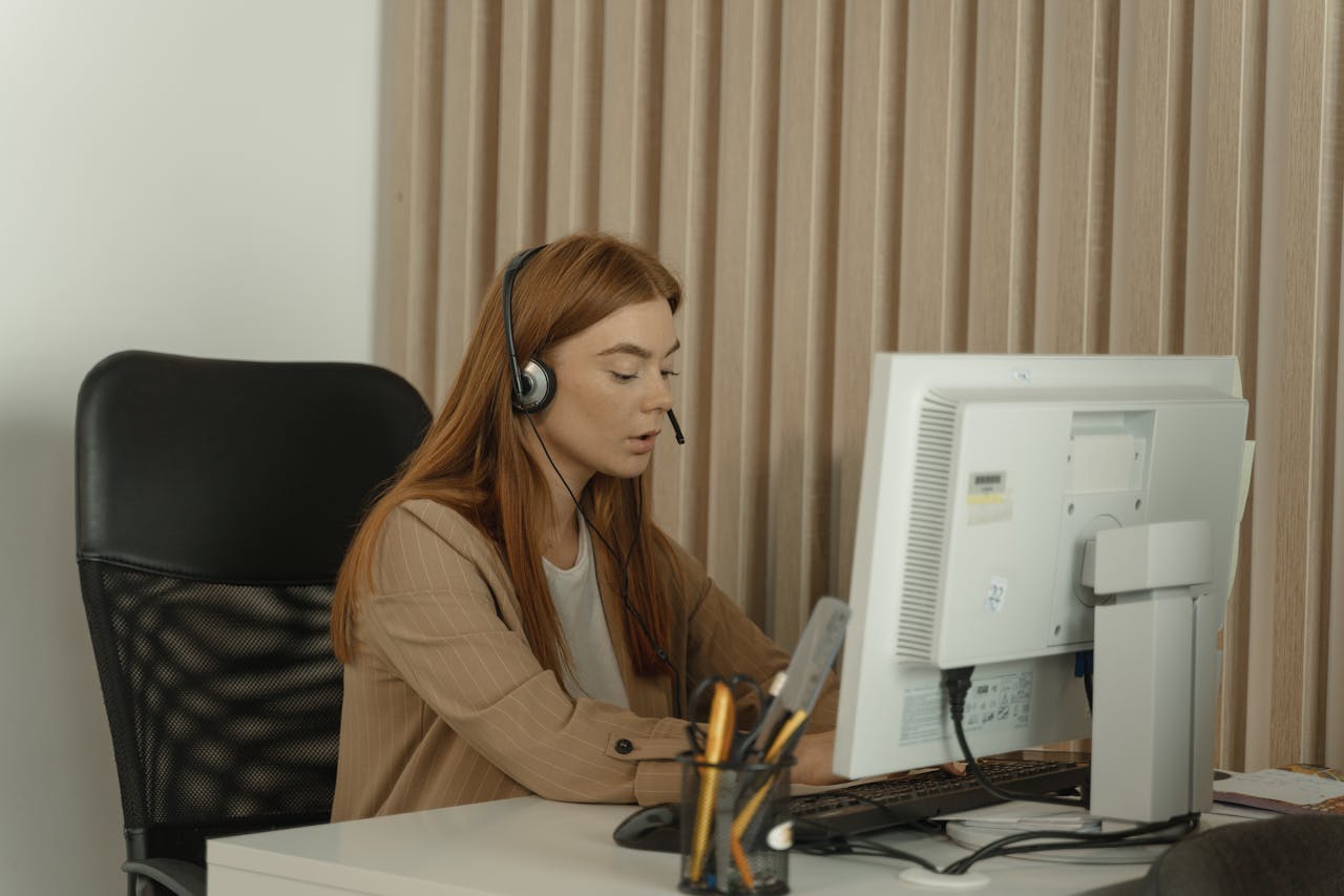 Female employee with headset working on desktop computer in office setting.